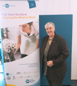 Fair Start Scotland participant Trish stands next to a Fair Start Scotland pop-up banner