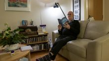 Older man in his well lit and warm living room. Looks very comfortable.